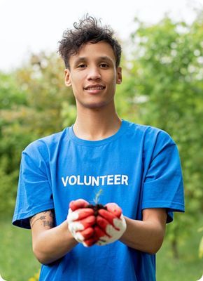Молодой человек в футболке с надписью 'VOLUNTEER' улыбается на фоне деревьев