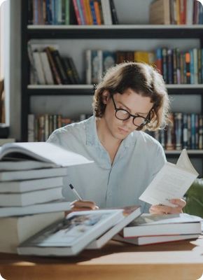 Человек в очках читает книгу за столом в библиотеке